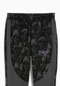 Sorte sweatpants med et kraniummønster, grå accenter, elastisk talje og en multicolor grafik på siden.
