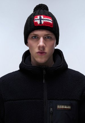 Black knitted beanie with a red, white, and blue Norwegian flag design and a pom-pom on top. Worn with a black fleece jacket featuring a logo.