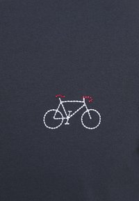 T-shirt en tissu bleu marine avec un motif de vélo brodé en blanc et des guidons rouges. Texture lisse, coupe décontractée.