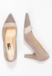 Spidse sko med en blanding af blød grå ruskind og en blank beige rem, med en tekstureret blokhæl for stabilitet og stil.