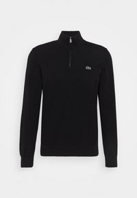 Pulover negru tricotat cu guler înalt și închidere cu fermoar pe jumătate. Prezintă un logo verde Lacoste pe piept. Mâneci lungi și manșete striate.