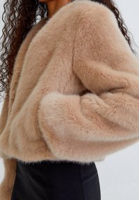 Ljusbeige faux fur-jacka med en kort design, rundade axlar och en mjuk textur. Har en bred krage och en avslappnad passform.