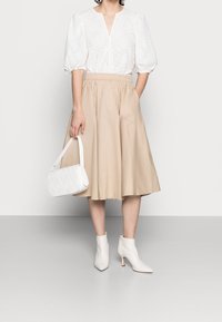 Witte oogjes blouse met pofmouwen, beige knie-lange geplooide rok, witte gewatteerde handtas en witte enkellaarsjes met een klein hakje.