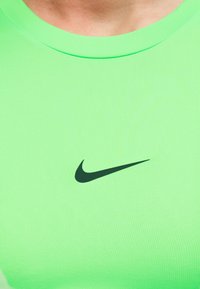 Κοντινό πλάνο ενός ατόμου που φοράει φωτεινό πράσινο πουκάμισο με μαύρο λογότυπο Nike Swoosh στο κέντρο του στήθους.