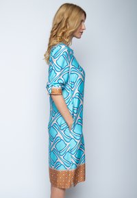 Niebieska i beżowa sukienka z odważnym geometrycznym wzorem, krótkimi rękawami, bocznymi kieszeniami i kontrastowym, wzorzystym dołem w ciepłych odcieniach.