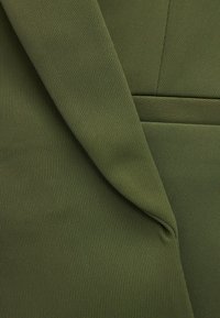 Tejido verde oliva con una textura estriada, que presenta secciones superpuestas y costuras rectas. El material parece suave y duradero.