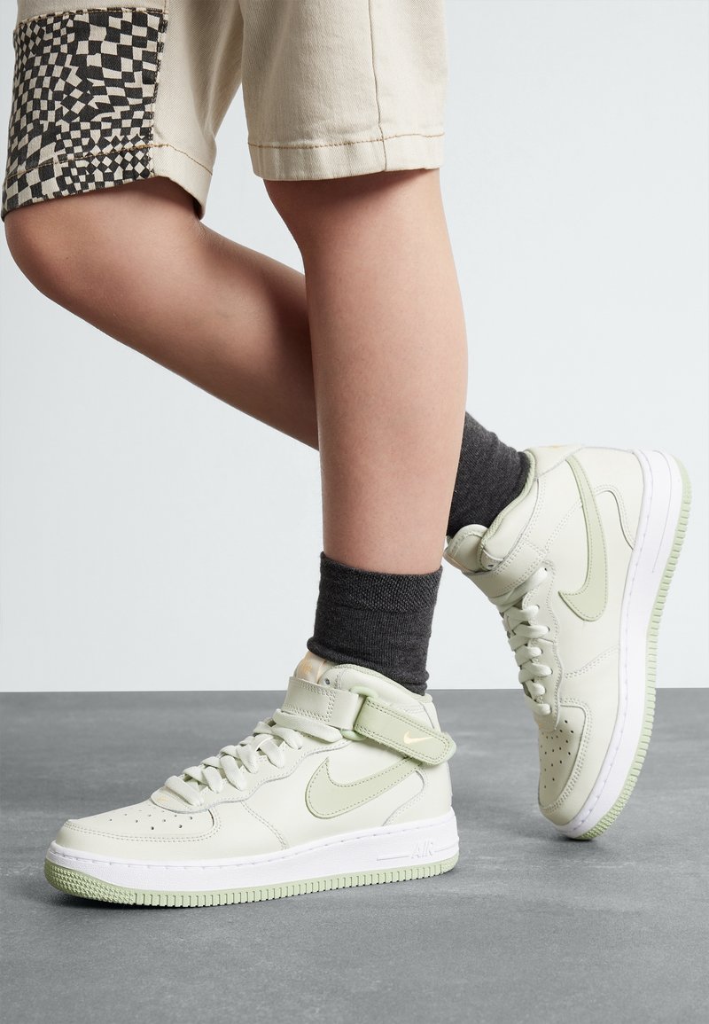 Zapatillas altas de cuero verde claro con suela blanca y acentos de menta. Presentan una correa, perforaciones y una superficie texturizada. Calcetines gris oscuro visibles en el tobillo.