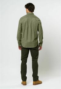 Cămașă cu mâneci lungi, de culoare verde măslin, dintr-un amestec de bumbac, cu guler și manșete cu nasturi. Asortată cu pantaloni verzi închis și cizme maro deschis.