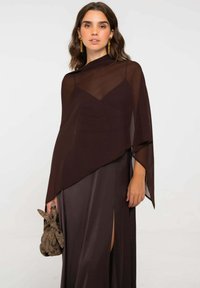 Vestido de noche marrón de satén con superposición transparente, escote en V, mangas largas y abertura lateral. Accesorios incluyen un bolso de mano marrón con estampado.