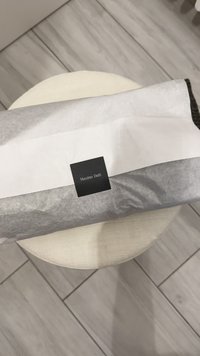 Rullet pakke indpakket i hvidt papir med en sort etiket med teksten "Massimo Dutti." Tekstureret overflade med en synlig mørk kant.