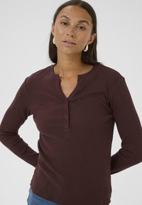 Burgundowa longsleeve w stylu henley z ryflowanym wzorem i zapięciem na trzy guziki, z okrągłym dekoltem i luźnym krojem.
