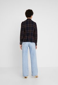 Marynarka w kratę w ciemnym niebieskim kolorze z czerwonymi i białymi liniami, zestawiona z jasnoniebieskimi dżinsami o szerokich nogawkach. Posiada mankiety zapinane na guziki oraz dopasowany krój.