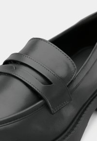 Mocassin noir en cuir avec une texture lisse, une tige peu profonde et deux bandes décoratives parallèles sur le cou-de-pied.