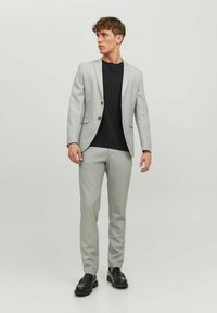 Gray blazer with two buttons, paired with gray trousers and a black t-shirt. Glossy black shoes complete the look. Smooth fabric texture.
