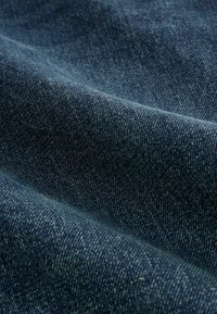 Tmavě modrá denímová tkanina s texturovaným vzorem, ukazující jemné barevné variace a drobné flíčky, složená tak, aby odhalila své povrchové detaily.