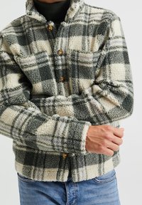 Vihreä- ja kermanvalkoinen ruudullinen fleecetakkipaita, jossa napilliset kiinnitykset, kaulus ja pehmeästi viimeistelty tekstuuri.