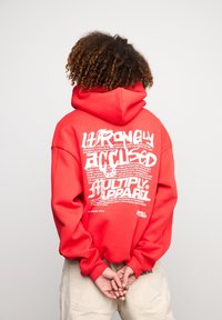 Roter Kapuzenpullover mit einem großen, weißen Grafiktextdesign auf der Rückseite. Verfügt über einen lockeren Schnitt, lange Ärmel und eine Kordelzugkapuze.