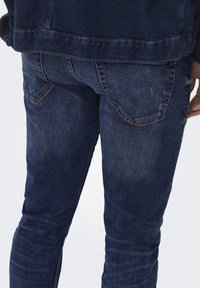 Mörkblå denimjeans med smal passform, med bakfickor med kontrasterande sömmar och viss blekning på tygstrukturen.