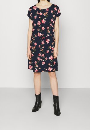Marineblaues Blumenkleid mit kurzen Ärmeln, das rosa Blumen und einen Kordelzug in der Taille aufweist. Schwarze Knöchelstiefel mit spitz zulaufender Zehe.