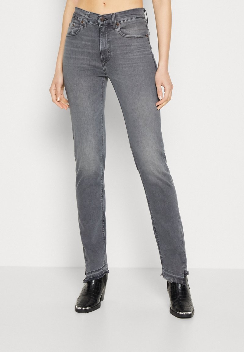 Jean gris foncé à taille haute avec une coupe droite. Présente un léger délavage, des ourlets effilochés et un design à cinq poches. Associé à des bottes à talons noires.