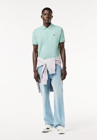 Polo shirt verde chiaro con colletto, abbinato a jeans azzurri e scarpe da ginnastica bianche. Un maglione grigio chiaro è annodato in vita.