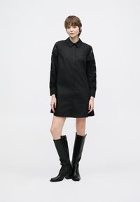 Fekete ingruhát hosszú csipkés ujjakkal, gombos elülső résszel és enyhén bővülő szegéllyel. Magas, fekete bőr magassarkú csizmával párosítva.