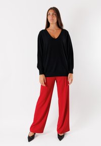 Maglione nero oversize con scollo a V, abbinato a pantaloni rossi a vita alta e gamba larga, e décolleté neri a punta. Tessuto morbido e vestibilità rilassata.