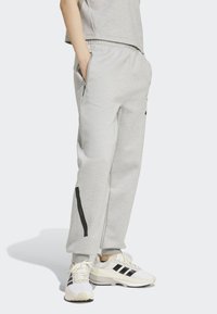 Pantaloni della tuta grigi con una vestibilità rilassata, dotati di tasche laterali e una striscia nera di accento lungo la gamba. Indossati con sneakers bianche.