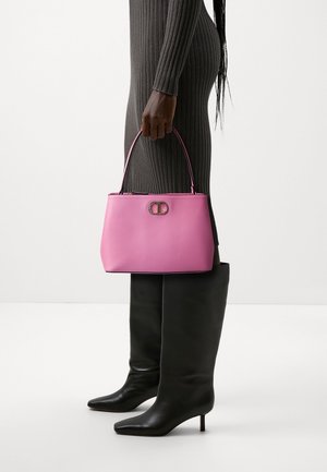 Woman in ribbed dark dress and black knee-high boots holding a pink handbag with a gold clasp at her side.