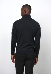 Dunkelblauer Strickpullover mit hohem Kragen, enganliegenden Ärmeln und gerippten Bündchen. Der Stoff wirkt glatt mit einem leichten Glanz.