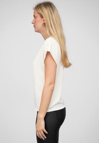Hvid kortærmet top med en afslappet pasform, tekstureret stof, rund halsudskæring og lige kant, parret med sorte skinny jeans.