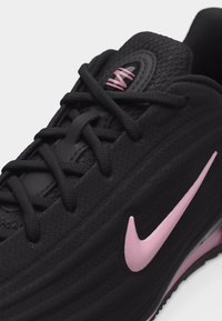 Μαύρο αθλητικό παπούτσι με ροζ λογότυπο Nike, μαύρα κορδόνια και ροζ λογότυπο "VAI" στη γλώσσα, εμφανιζόμενο από κοντινή κεκλιμένη κορυφαία όψη.