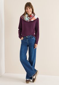 Purple knit sweater, blue wide-leg jeans, and brown sneakers with white accents. Colorful patterned scarf draped around the neck.