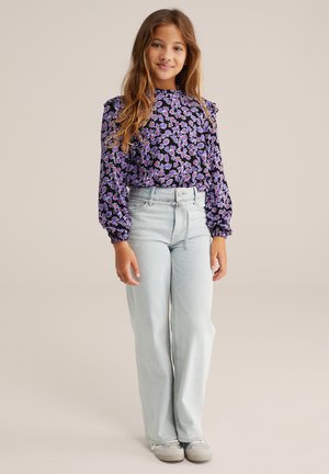 Bluse med blomsterprint i sort og lilla, med lange ærmer og elastiske manchetter. Båret med lyseblå brede jeans og grå sko.