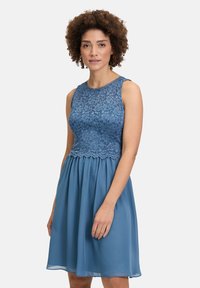 Een mouwloze jurk met een blauwe kanten bovenkant en een vloeiende chiffonrok, gekenmerkt door een scalloped zoom en een ronde halslijn.