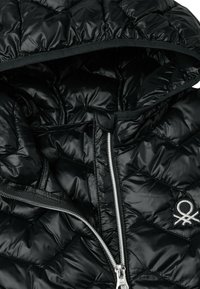 Černá prošívaná péřovka s uzávěrem na zip, disponující kapucí a decentním logem na hrudi. Materiál má hladkou, lesklou strukturu.