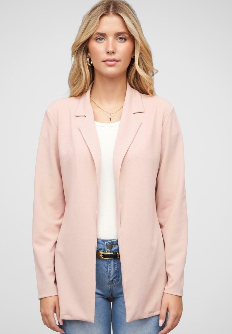 Lyserød blazer med lange ærmer, blød tekstur, åben front og enkle revers, båret over en hvid top og blå jeans.
