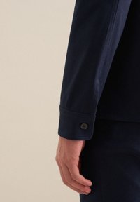Manica di camicia blu navy con polsino a bottone, tessuto liscio e vestibilità su misura, che mostra cuciture precise e linee pulite.