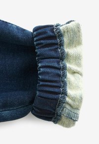 Jambe de pantalon en denim bleu foncé retroussée pour révéler une doublure polaire douce gris clair avec des coutures visibles et des bords légèrement effilochés.