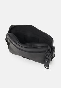 Borsa a tracolla in pelle nera con scomparto principale con zip aperto, tasca frontale con zip e cinturino regolabile con fibbia in metallo.