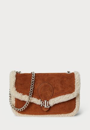 Bruine suede handtas met een crèmekleurige nepbont trim, zilveren kettinghengsel en een opvallend circulair logo detail aan de voorkant. Rechthoekige vorm.