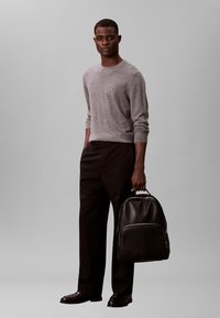 Grijze gebreide trui, zwarte broek en zwarte leren rugzak. Eenvoudig ontwerp, medium dikte, gladde textuur en minimale details.