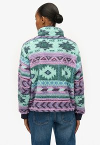 Pull polaire avec un col montant, présentant des motifs géométriques en bleu sarcelle, lavande et violet, avec une texture douce et des poignets côtelés.