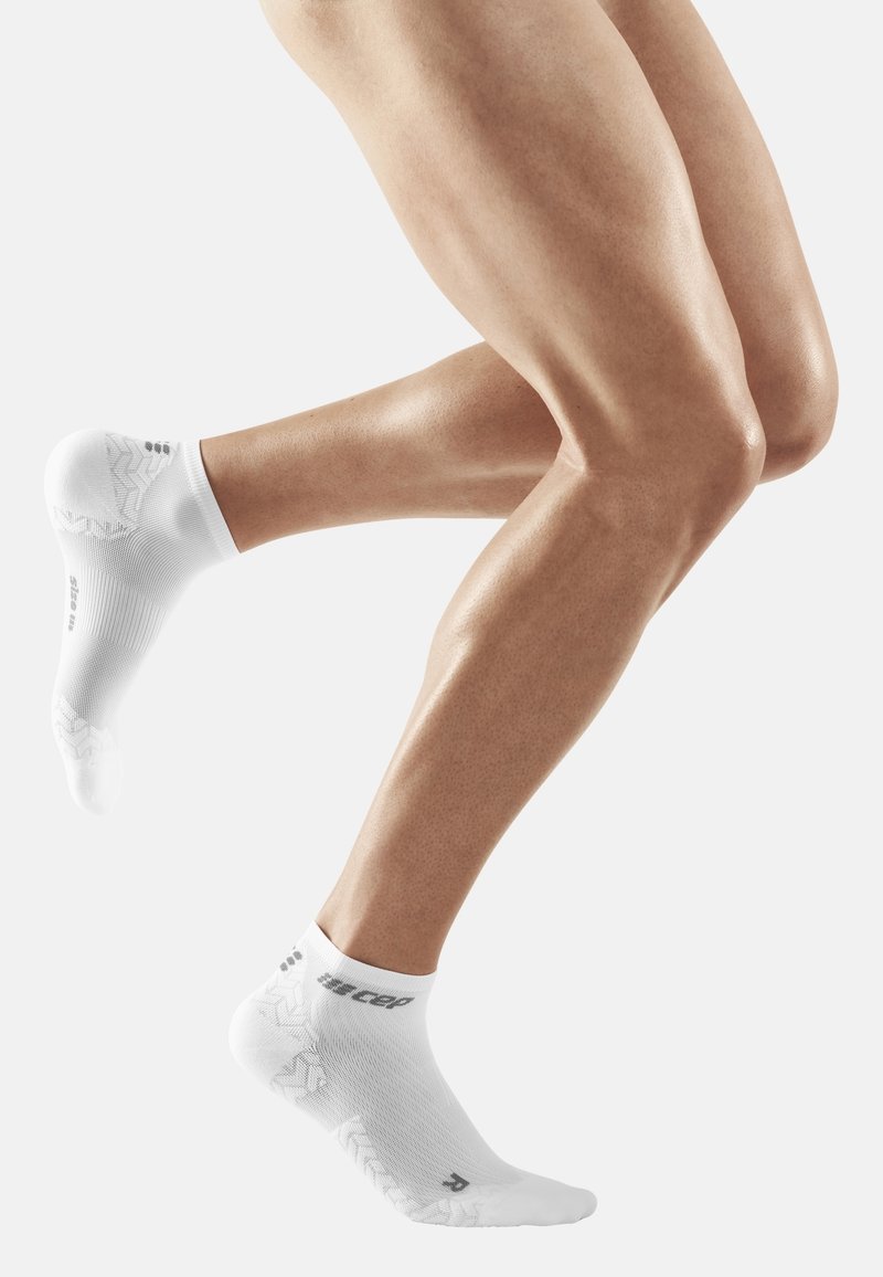 White ankle socks with a textured design. Features a logo on the cuff and a patterned sole. Smooth fabric with a close fit.