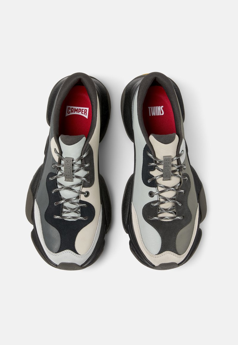 Schwarze und graue Sneakers mit dicken Gummisohlen, die ein Mischmaterialdesign aufweisen, strukturierte Akzente haben und rote Innensohlen mit dem Aufdruck "CAMPER" und "TWINS".