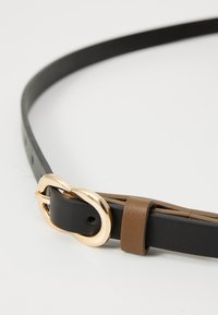 Cintura in pelle nera e marrone con fibbia a doppio anello in tono oro e un design elegante, con cuciture visibili e notches regolabili.