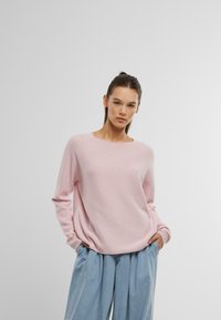 Lichtroze gebreide trui met een ontspannen pasvorm, ronde hals en lange mouwen, gecombineerd met losse blauwe denim broeken. Glad textuur.