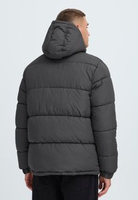 Puffjakke i mørkegrå med hætte, med quiltede sektioner, elastiske manchetter og en afslappet pasform, designet til varme og komfort.