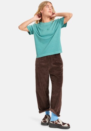 T-shirt in cotone teal, vestibilità ampia, pantaloni in velluto a coste marroni a coste, calzini blu e scarpe slip-on marroni con motivo a macchie di mucca.