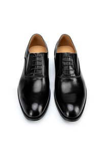Chaussures habillées en cuir noir avec une texture lisse, bout arrondi, design à cinq œillets et doublure intérieure contrastante de couleur marron clair.